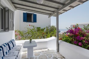 A white outdoor seating area with a table, a sofa, and a view of the sea. - Holiday Home 'Mykonos Serenity 1' with Shared Pool, Wi-Fi and Air Conditioning (Mykonos)