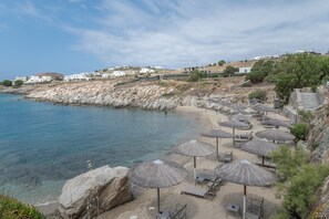 A beach with umbrellas, lounge chairs, and a rocky coastline. - Holiday Home 'Mykonos Serenity 1' with Shared Pool, Wi-Fi and Air Conditioning (Mykonos)