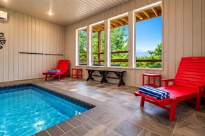 A swimming pool area with red chairs and a table, large windows with a view of greenery, and a tiled floor. - Hilltop Dreamin': Life's Better Up Here (Sevierville)