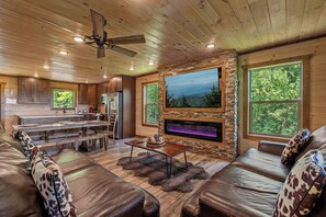 Ein geräumiges Wohnzimmer mit Kamin aus Stein, Ledersofas und einem großen Fernsehbildschirm.