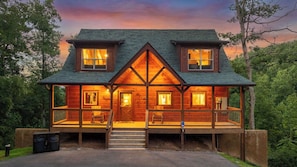 A two-story wooden cabin with a porch, a covered front entrance, and a fenced deck area. - Hilltop Dreamin': Life's Better Up Here (Sevierville)