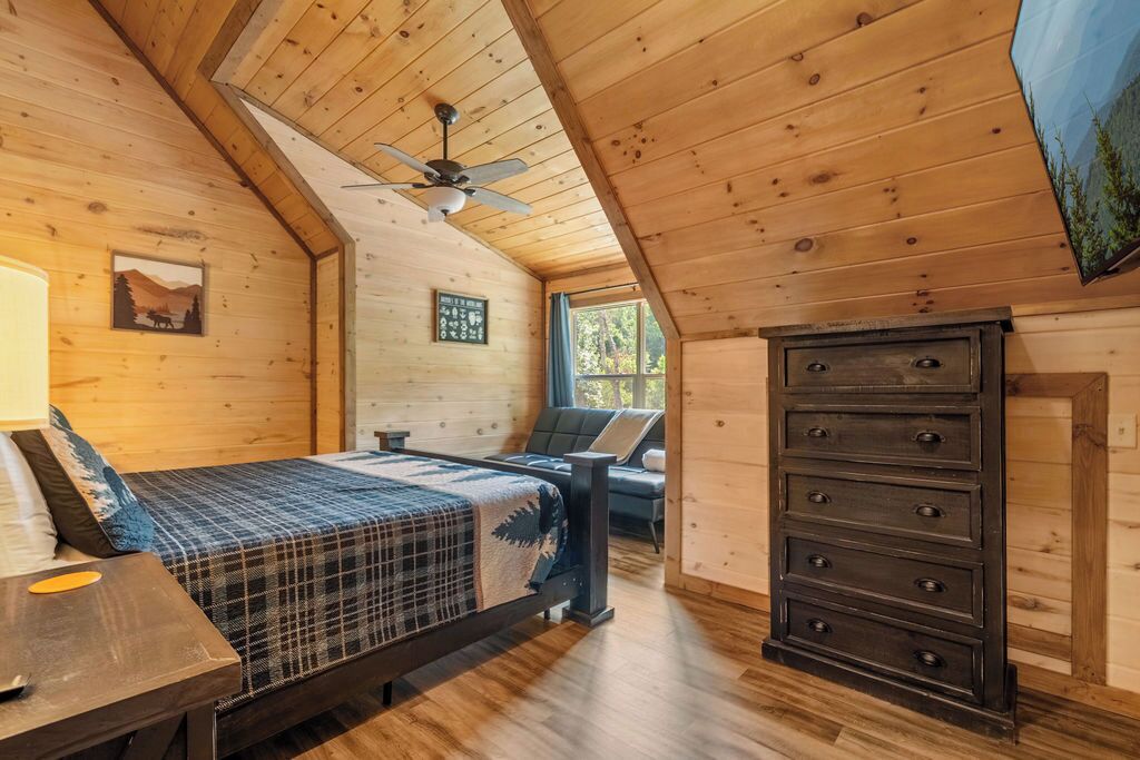 Une chambre confortable dans un chalet, avec un lit, une commode et un ventilateur de plafond.