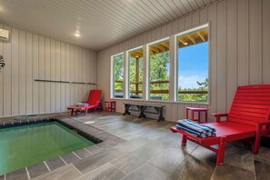 Ein Poolbereich mit Whirlpool, roten Liegestühlen und Blick auf Bäume durch große Fenster.
