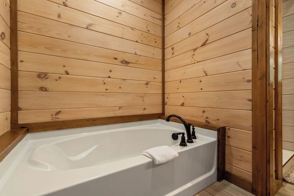 A wooden-paneled bathroom with a white bathtub, a black faucet, and a white towel.