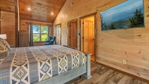 Un dormitori de cabana de fusta amb un llit, una cadira i una finestra gran.