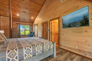 Ein Schlafzimmer einer Holzhütte mit einem Bett, einem Sessel und einem großen Fenster.