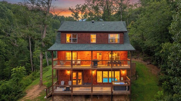 A two-story log cabin with a balcony and a pool, surrounded by dense forest. - Hilltop Dreamin': Life's Better Up Here (Sevierville)