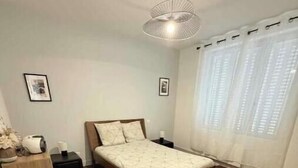 Una camera da letto con pavimento in legno, un letto con testiera, un comodino, una lampada e una finestra con tende.