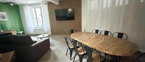 A dining area with a round wooden table and chairs, a flat-screen TV mounted on the wall, and a green accent wall.