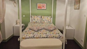 Un letto a baldacchino con copriletto floreale, un comodino con una lampada e una piccola mensola con un oggetto a forma di cuore.