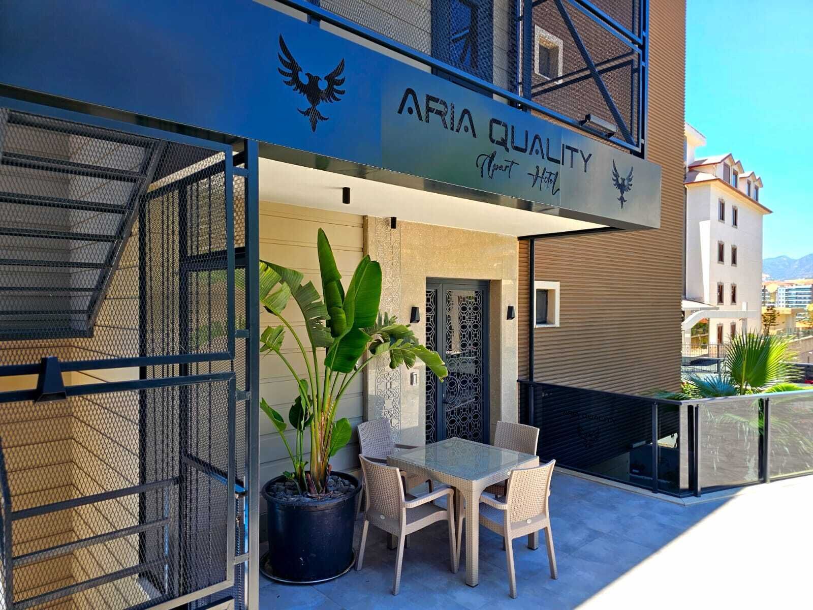 A modern building with a sign reading 'ARIA QUALITY Hotel' and a balcony with a table and chairs.