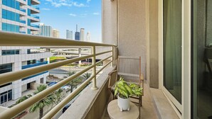 A balcony with a railing, a potted plant, a chair, and a view of a cityscape with modern buildings. - Bloomfields Studio in Manchester Tower (Dubai)