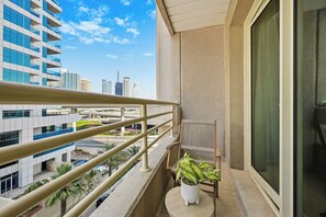 Ein Balkon mit Geländer, einem Blumentopf, einem Stuhl und Blick auf eine Skyline mit modernen Gebäuden.
