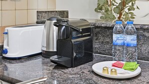 A kitchen counter with a toaster, a coffee maker, two water bottles, and a plate with condiments. - Bloomfields Studio in Manchester Tower (Dubai)