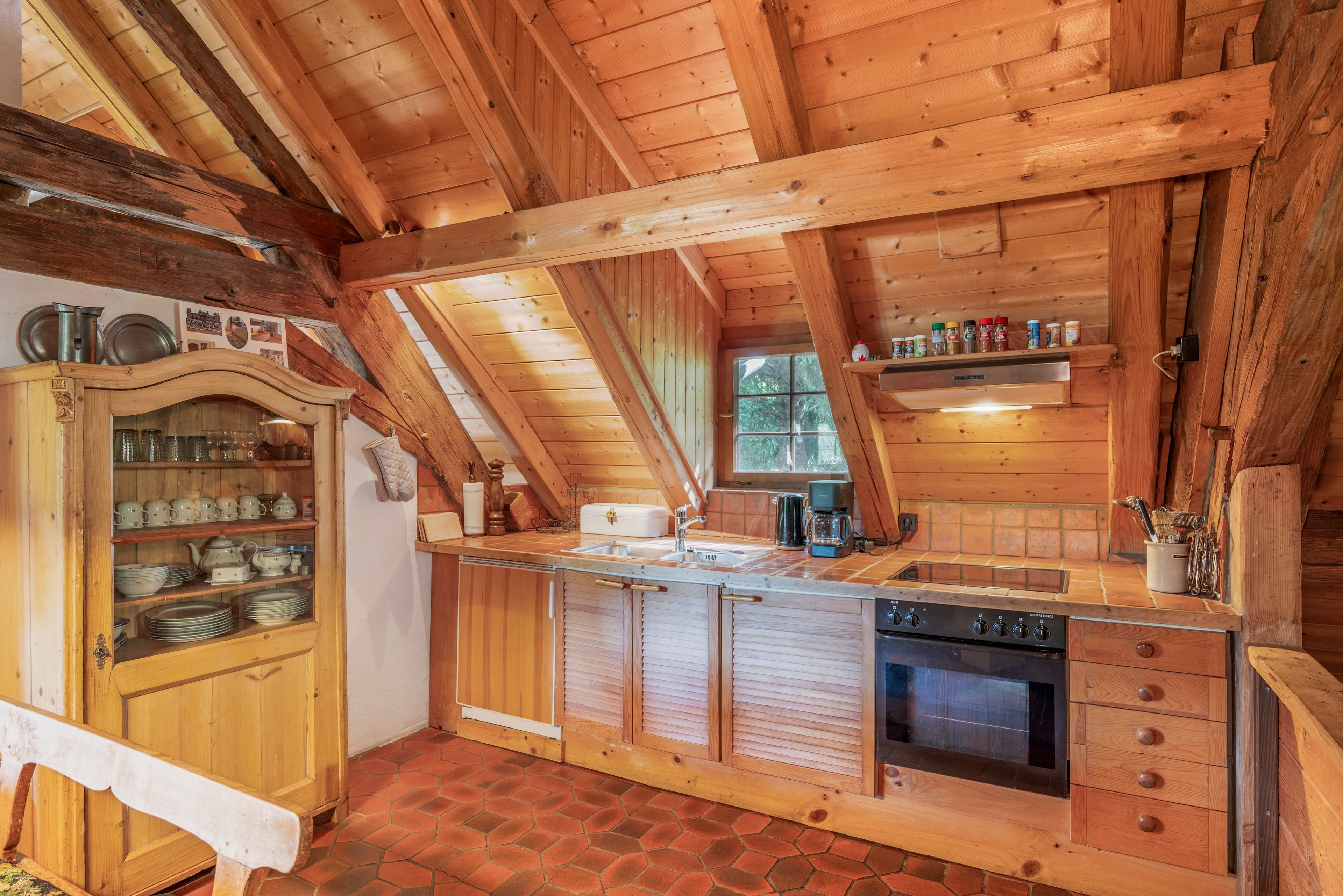 Eine Holzküche mit schrägen Wänden, einem eingebauten Schrank, einem Herd und einem Fenster.