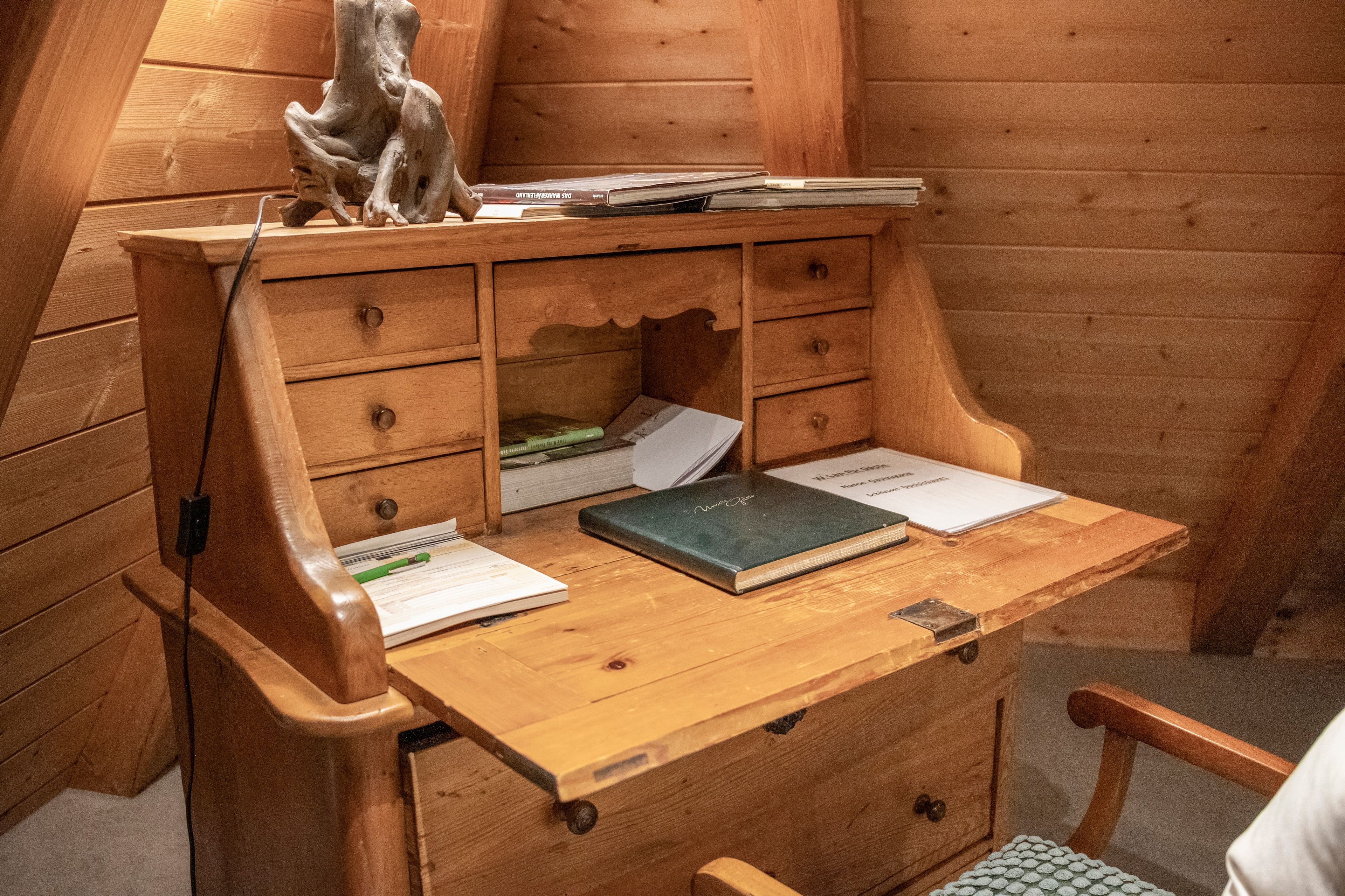 A wooden desk with drawers, a book, papers, and a decorative object.