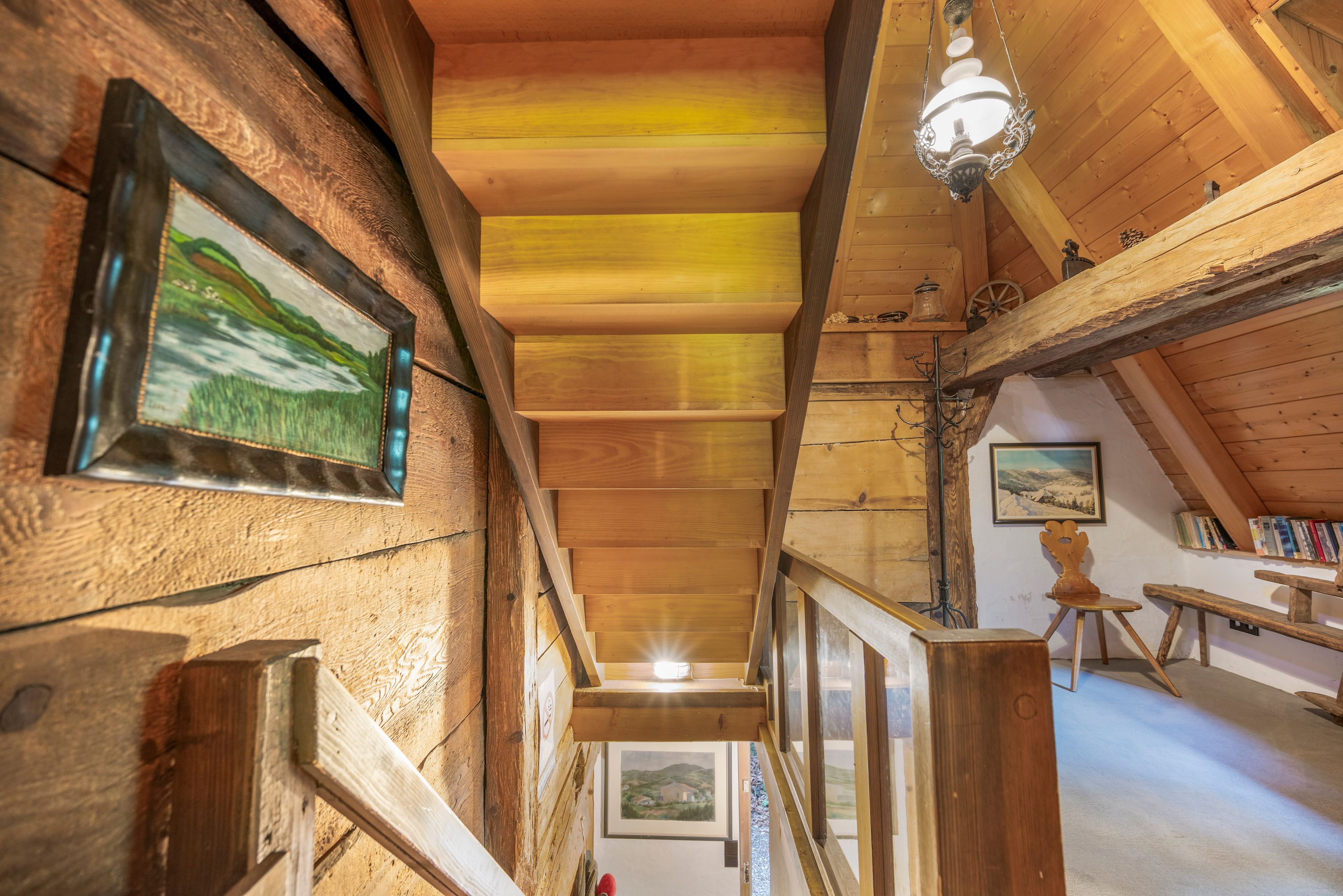 Een houten interieur met een trap, kunstwerken in lijsten en een hanglamp.