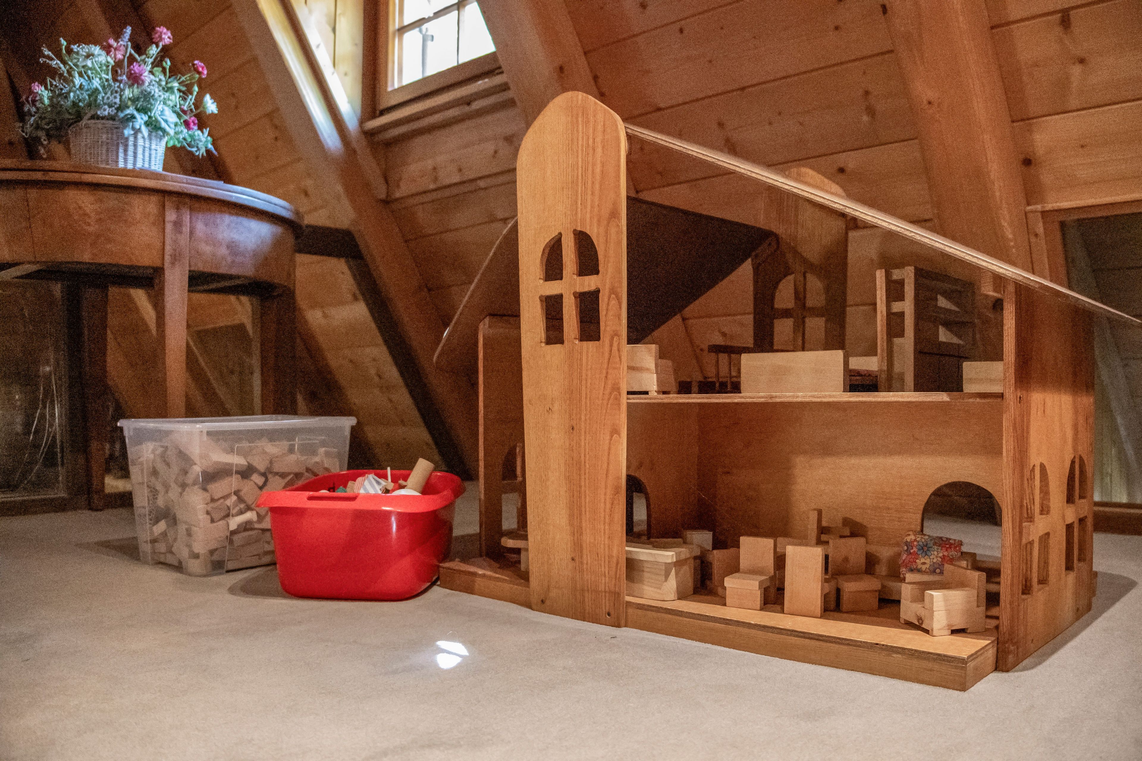 Une maquette d’une maison en bois avec un toit à deux versants, une poubelle rouge et un récipient en pierre.