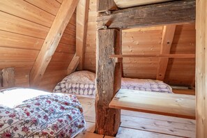Een houten interieur met een stapelbed, beddengoed met een patroon, en een schuine plafond.