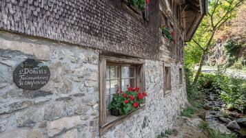 Ein Steinhaus mit traditionellem Satteldach, einem Fenster mit roten Blumen und einer steinernen Platte mit Kontaktinformationen.