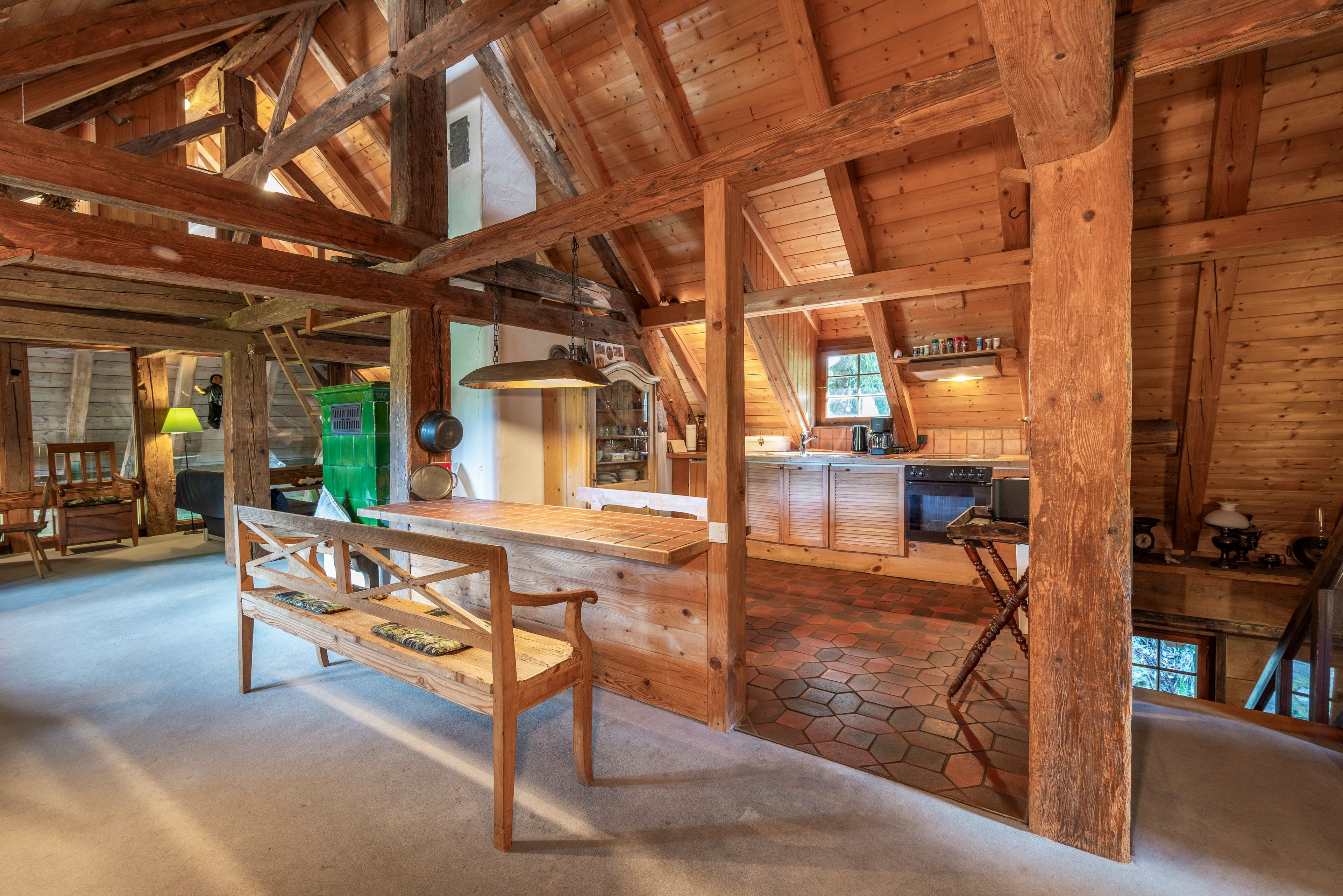 A rustic wooden interior with a high ceiling, a dining area with a bench, and a kitchen with a stove.