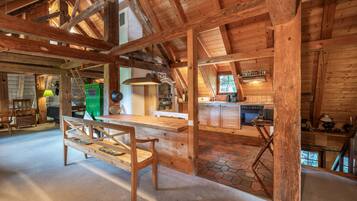 A rustic wooden interior with a high ceiling, a dining area with a bench, and a kitchen with a stove.