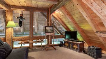 A cozy attic room with a wooden ceiling, a television, a painting on easel, and a plush sofa.