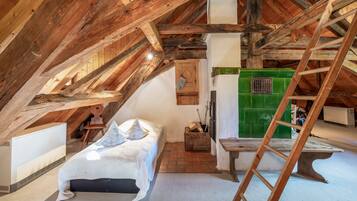 Ein Schlafzimmer im Spitzboden mit schrägem Dach, einer Holzleiter, einem Bett, einem kleinen Tisch und einem grünen Gerät.