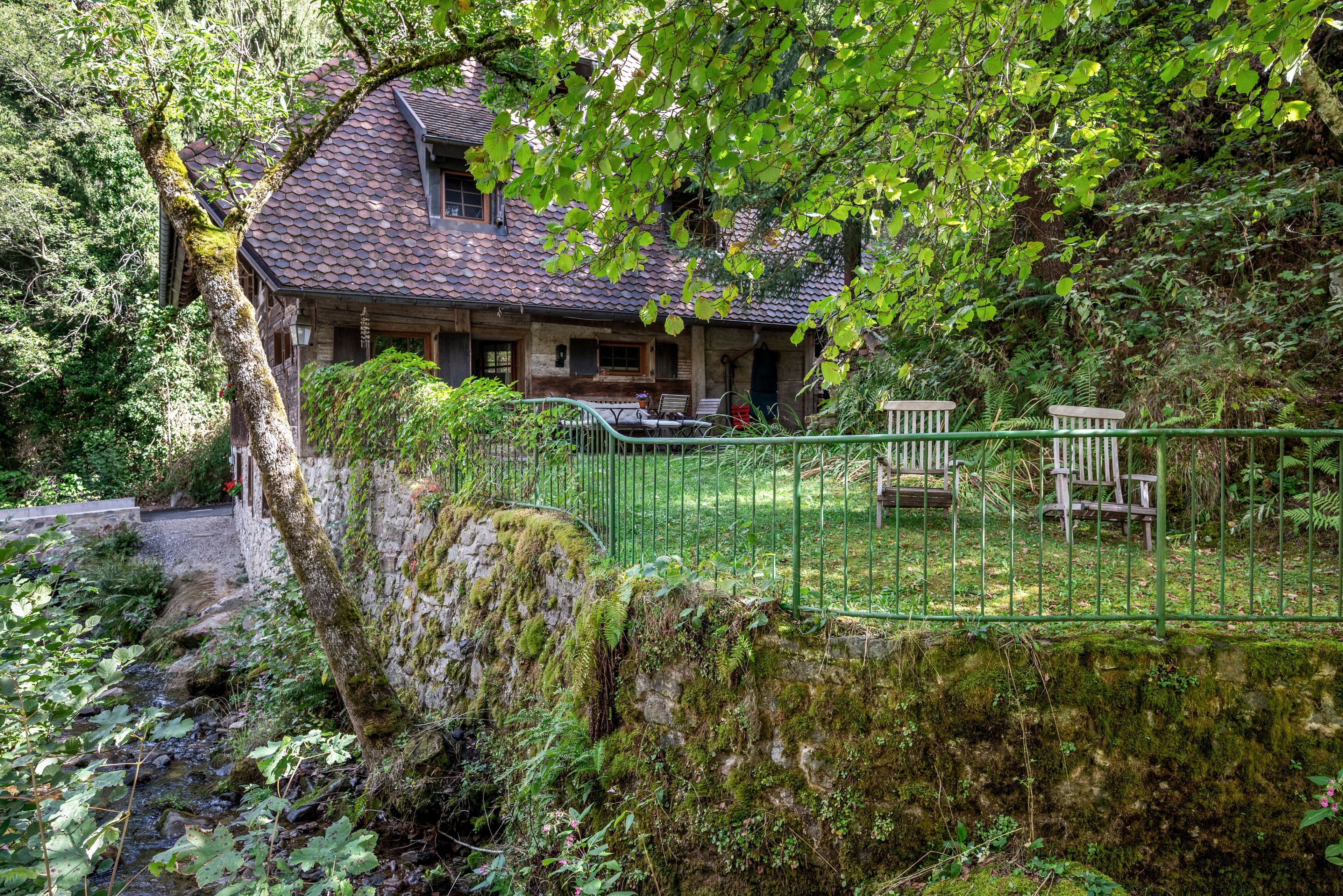 Ein rustikales Haus mit Stein Fundament, einem Ziegeldach und einem grünen Metallzaun.