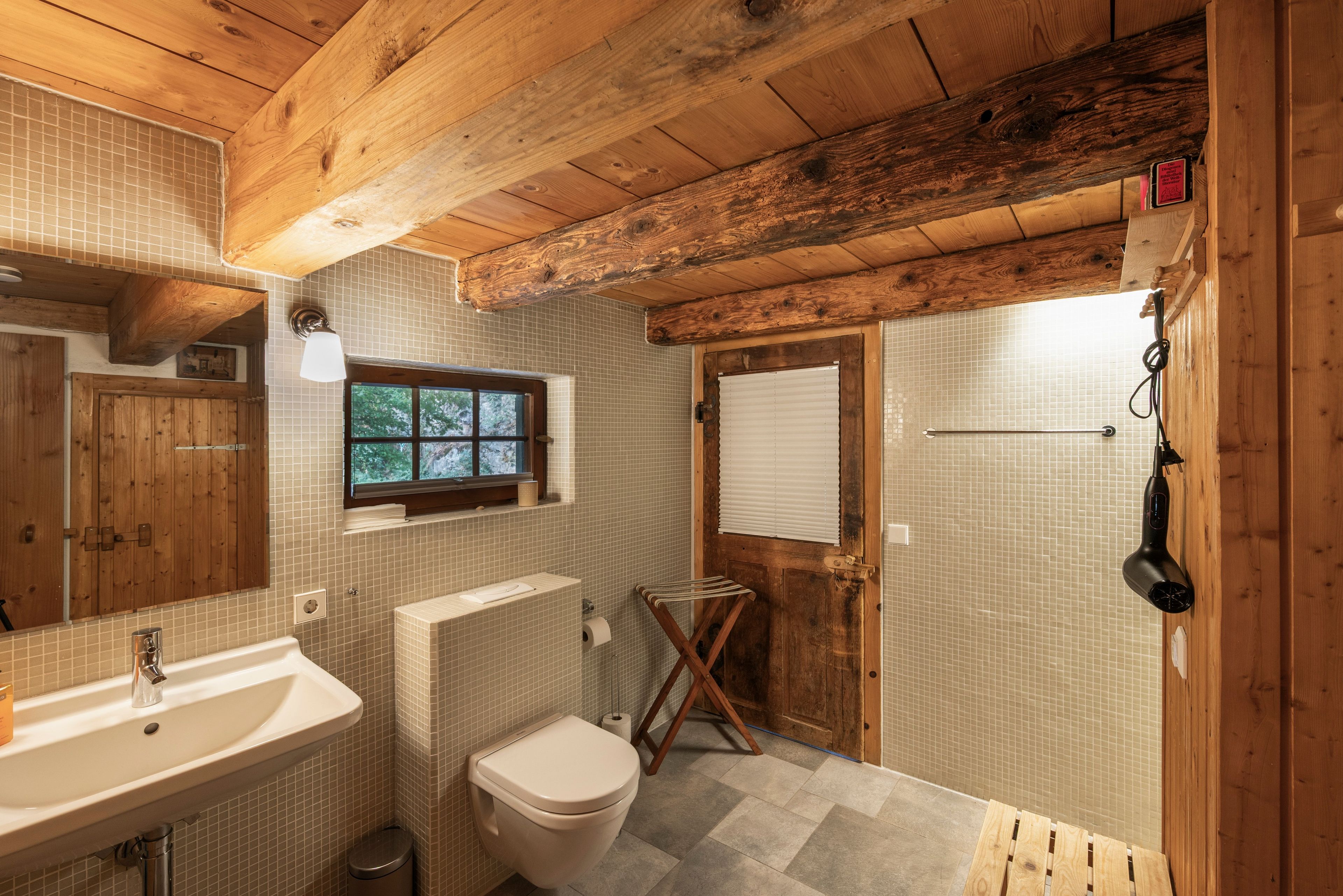 Ein Badezimmer mit Holzboden, einem Waschbecken, einer Toilette und einem Fenster.
