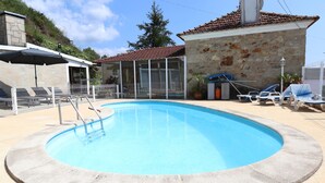 Ein Pool mit Steinmauer, einer überdachten Sitzgelegenheit und Blick auf ein Steinhaus.