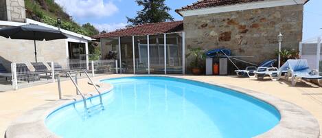 A swimming pool with a stone wall, a covered seating area, and a view of a stone building.