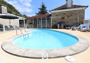 A swimming pool with a stone wall, a covered seating area, and a view of a stone building. - MyStay - Casa Pedrosa (Viana do Castelo)