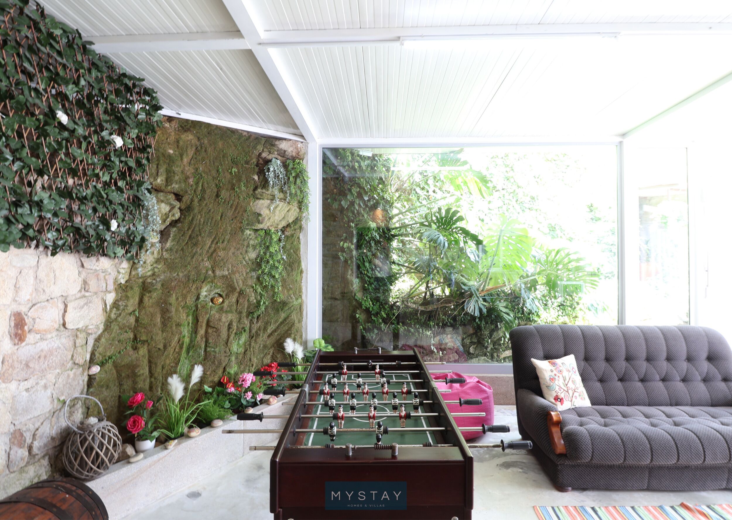 A cozy indoor space with a foosball table, a sofa, and a stone wall adorned with greenery.
