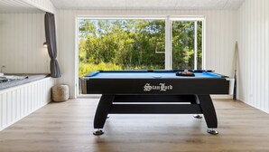 Une table de billard placée devant une porte vitrée, offrant une vue sur une forêt.