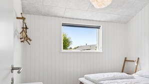 Une chambre à coucher avec un lit, une fenêtre, un plancher en bois et un mur blanc.