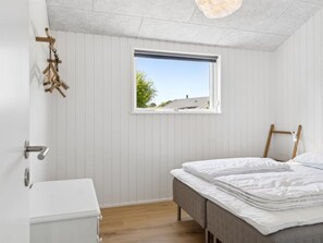 Ein Schlafzimmer mit Bett, Fenster, Holzboden und weißer Wand.