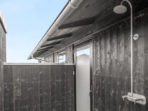 Une façade en bois, une gouttière métallique sur le toit, une clôture en bois et une pomme de douche en métal.