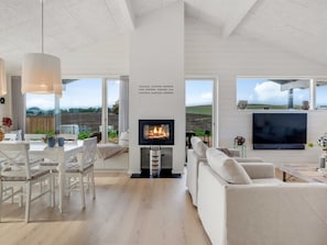 A spacious living area with a fireplace, white furniture, and large windows offering a view of the outdoors. - "Pia" - 350m from the sea by Interhome (Knebel)