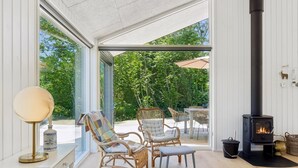 Une pièce spacieuse avec de grandes fenêtres, des meubles en osier, une table et un poêle à bois.