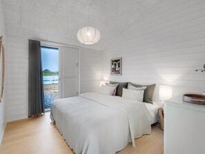 A bedroom with a bed, pillows, a bedside table, a lamp, and a view of the outdoors through a door. - "Pia" - 350m from the sea by Interhome (Knebel)