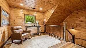 A wooden cabin interior with a loft bedroom, a rocking chair, a window with a view, and a small table with a vase. - Thunderhead Mountain Lodge- Amazing Views, Amazing Private Pool & Game Room (Sevierville)