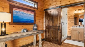 A wooden interior with a painting of mountains, a wooden door, a mirror, and a wooden bench with a lamp and lantern. - Thunderhead Mountain Lodge- Amazing Views, Amazing Private Pool & Game Room (Sevierville)