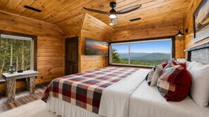 A wooden cabin bedroom with a large bed, a painting, a window with a mountain view, and a ceiling fan. - Thunderhead Mountain Lodge- Amazing Views, Amazing Private Pool & Game Room (Sevierville)