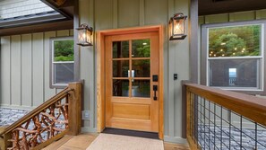 A wooden front door with a glass panel, a wooden staircase with a metal railing, and two wall-mounted lanterns. - Thunderhead Mountain Lodge- Amazing Views, Amazing Private Pool & Game Room (Sevierville)