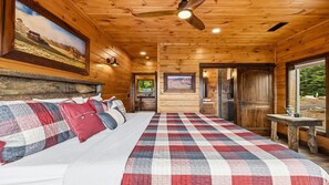 A wooden cabin interior with a bed, a ceiling fan, and a view of the outdoors. - Thunderhead Mountain Lodge- Amazing Views, Amazing Private Pool & Game Room (Sevierville)