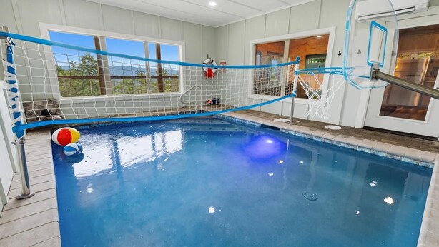 An indoor swimming pool with a blue water surface, a rope safety net, and a beach ball. - Thunderhead Mountain Lodge- Amazing Views, Amazing Private Pool & Game Room (Sevierville)
