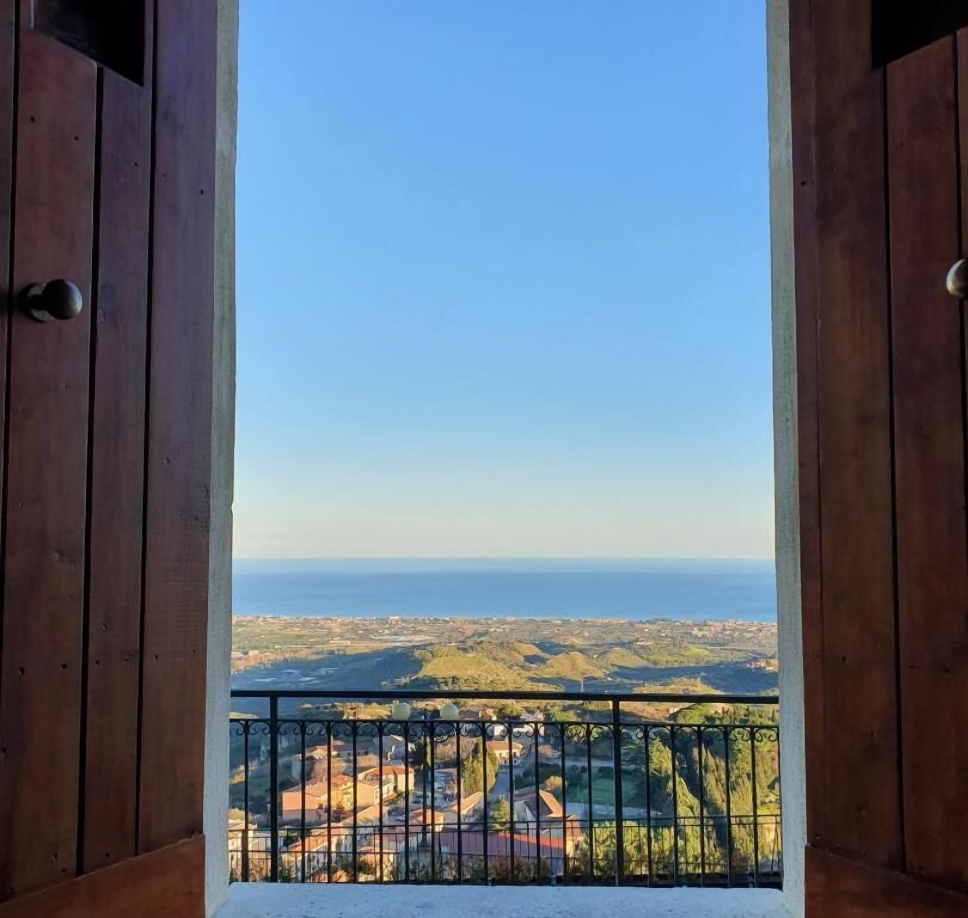 Een houten balkon met een metalen hekwerk, met uitzicht op zee en het verre landschap.