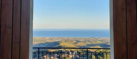 Un balcón de madera con barandilla de metal, que ofrece vistas al mar y el paisaje distante.