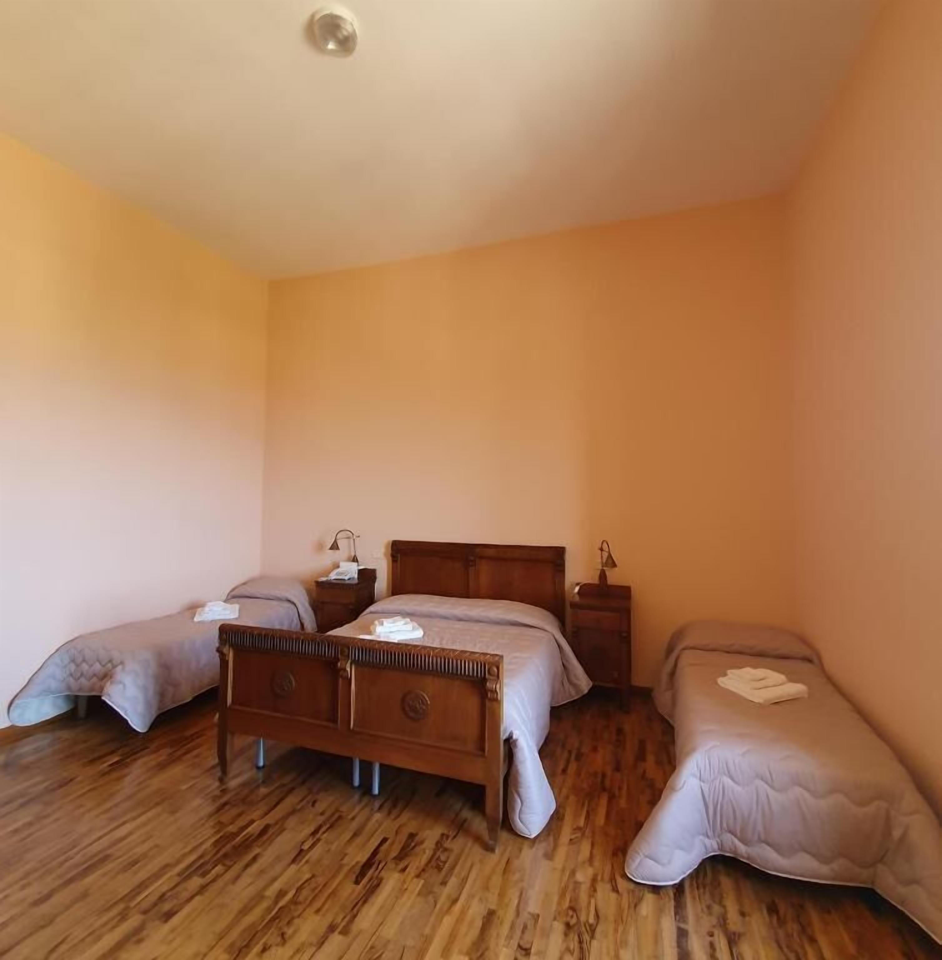Een kamer met een houten vloer, een groot bed met hoofdeinde, twee nachtkastjes en een eenpersoonsbed aan de rechterkant.